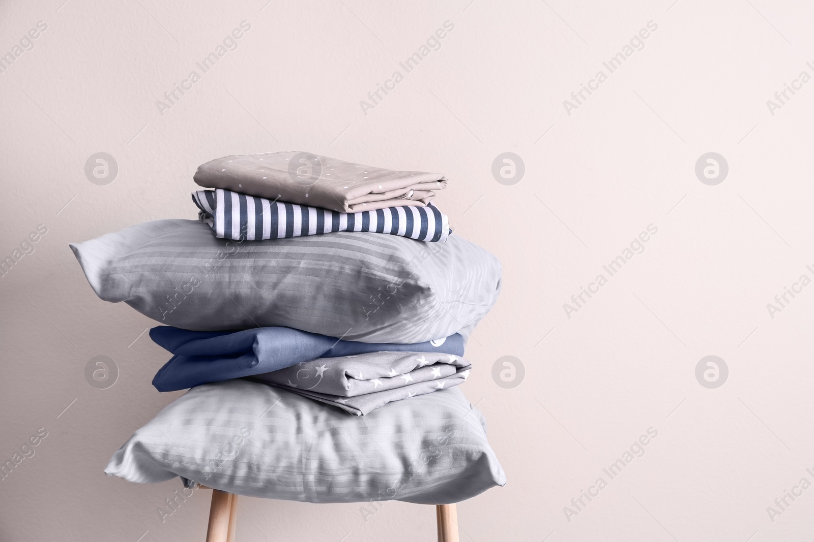 Photo of Stack of clean bed sheets and pillows on stool near beige wall. Space for text