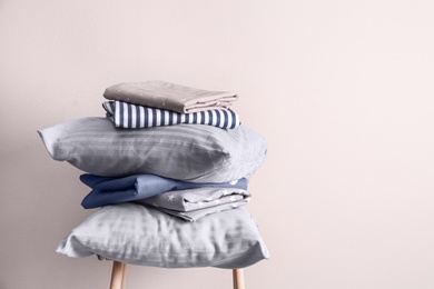 Stack of clean bed sheets and pillows on stool near beige wall. Space for text