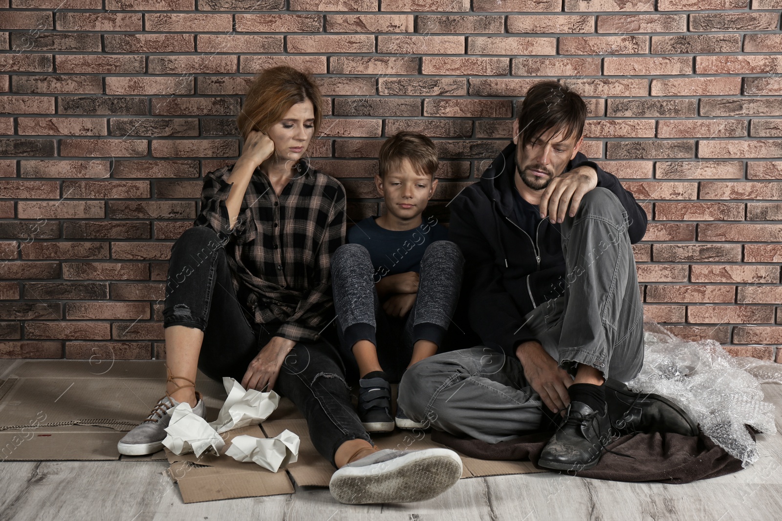 Photo of Poor homeless family sitting on floor near brick wall