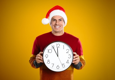 Photo of Man in Santa hat with clock on yellow background. Christmas countdown
