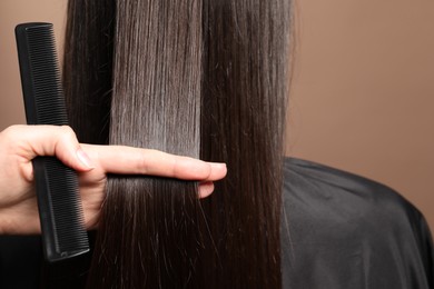 Photo of Hairdresser styling client's hair on light brown background, closeup