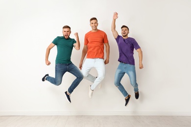 Photo of Group of young men in jeans and colorful t-shirts jumping near light wall
