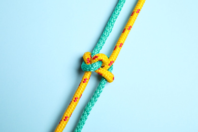 Photo of Colorful ropes with knot on light blue background, top view. Unity concept