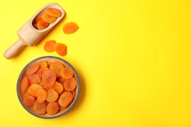 Bowl and scoop of dried apricots on color background, top view with space for text. Healthy fruit