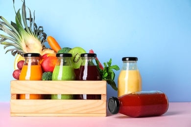 Bottles with delicious colorful juices and fresh ingredients in wooden crate on pink table