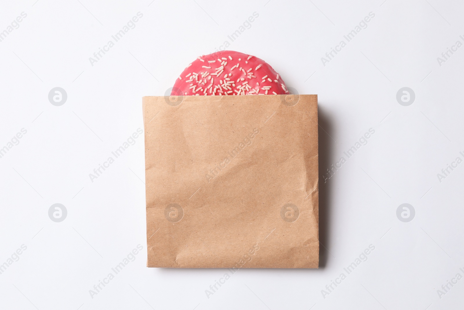 Photo of Paper bag with glazed doughnut on white background, top view. Space for design