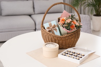 Wicker basket with gifts near sweets on table indoors. Space for text