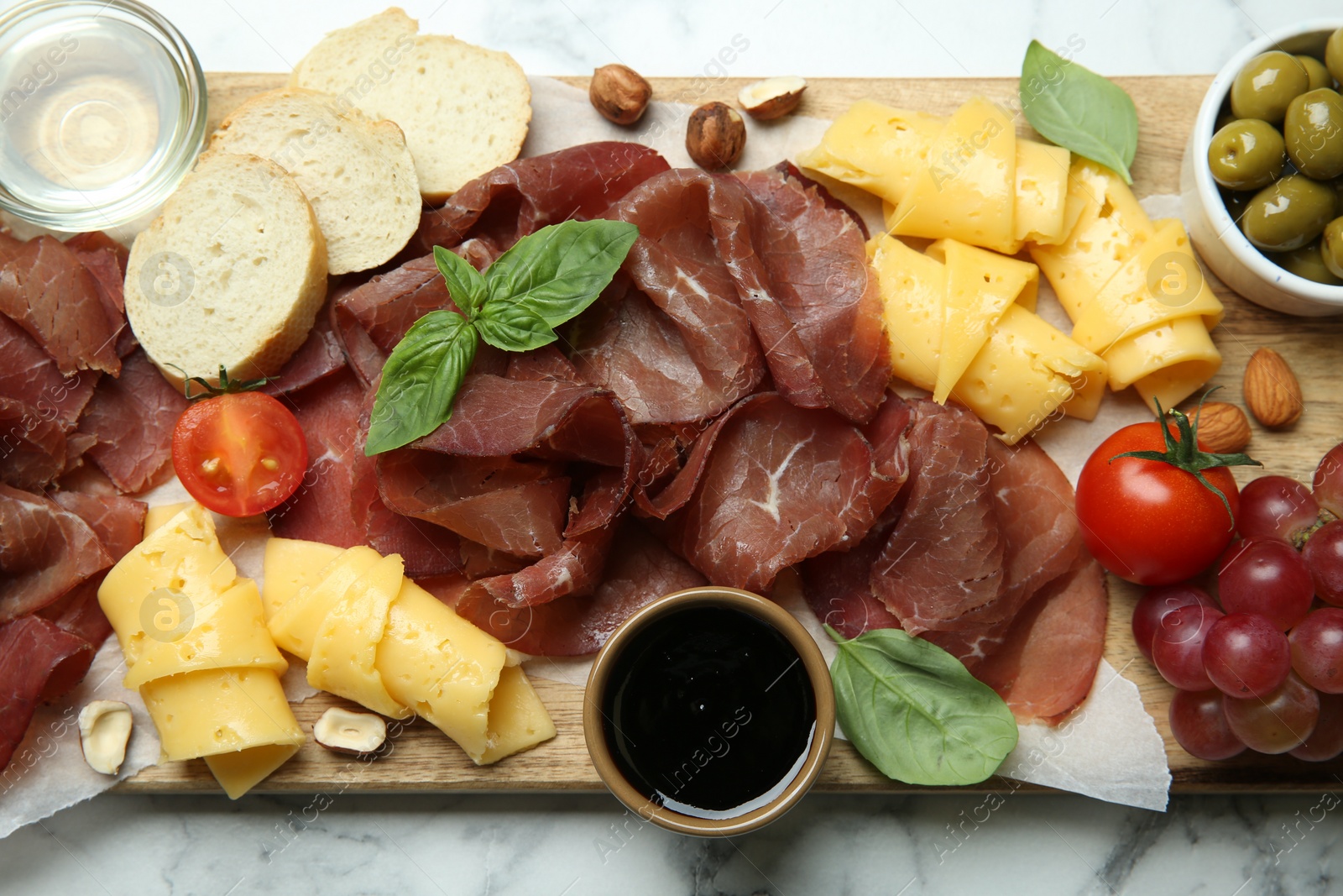 Photo of Charcuterie board. Delicious bresaola and other snacks on white marble table, top view