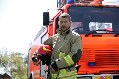 Portrait of firefighter in uniform with helmet near fire truck outdoors