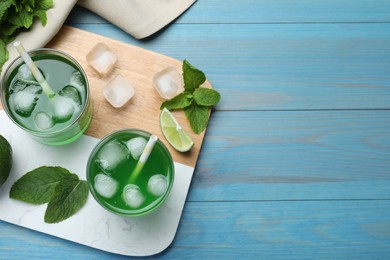 Photo of Delicious mint liqueur with green leaves and ice cubes on turquoise wooden table, flat lay. Space for text