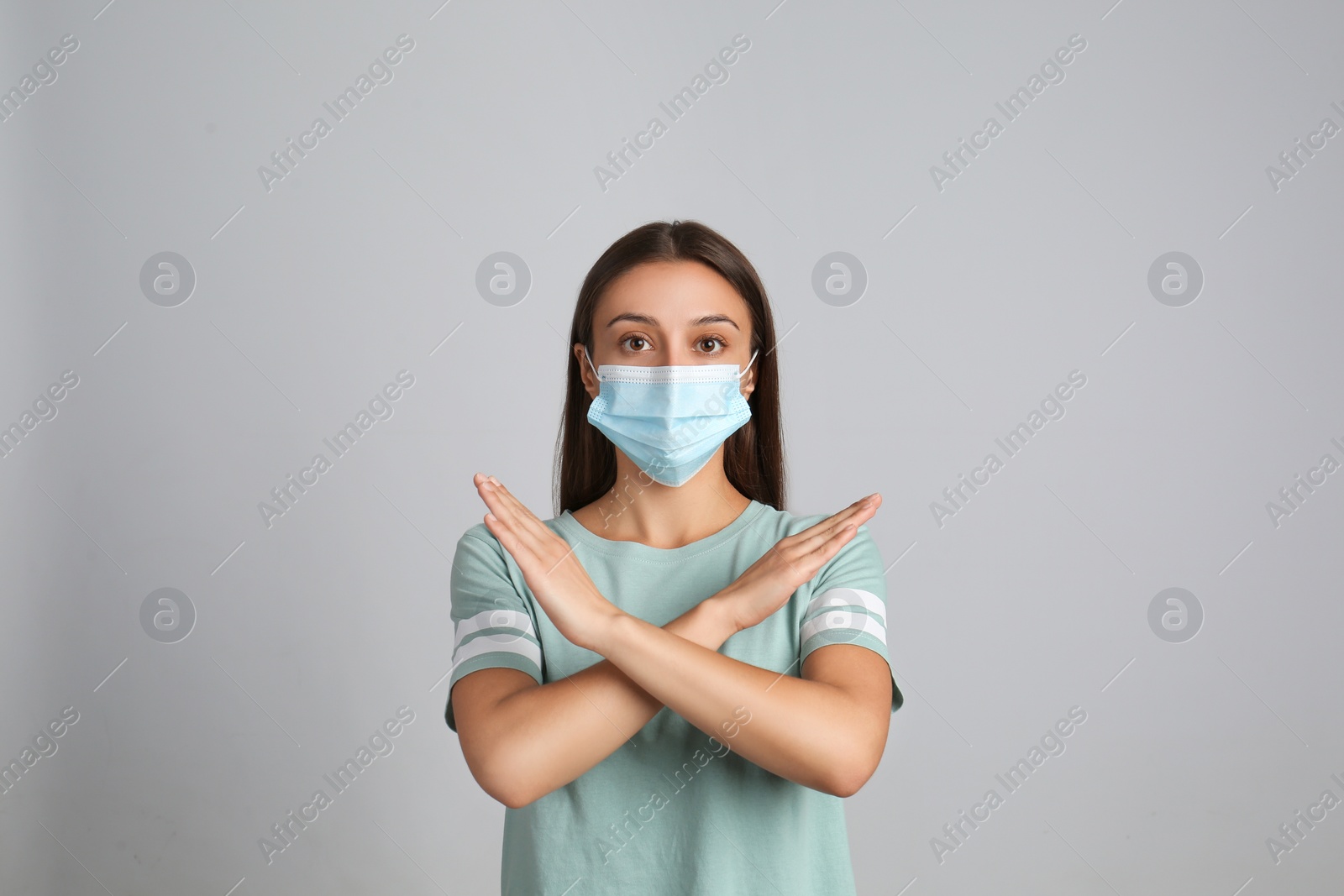 Photo of Woman in protective mask showing stop gesture on grey background. Prevent spreading of COVID‑19