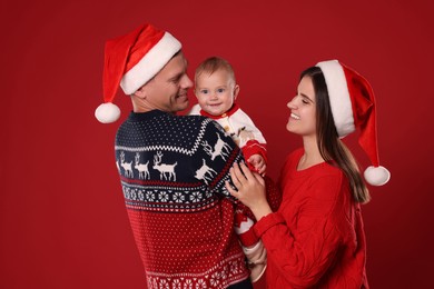 Happy couple with cute baby in Christmas outfits and Santa hats on red background