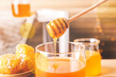 Dripping tasty honey from dipper into glass on table, closeup