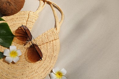 Flat lay composition with stylish sunglasses and wicker bag on sand. Space for text