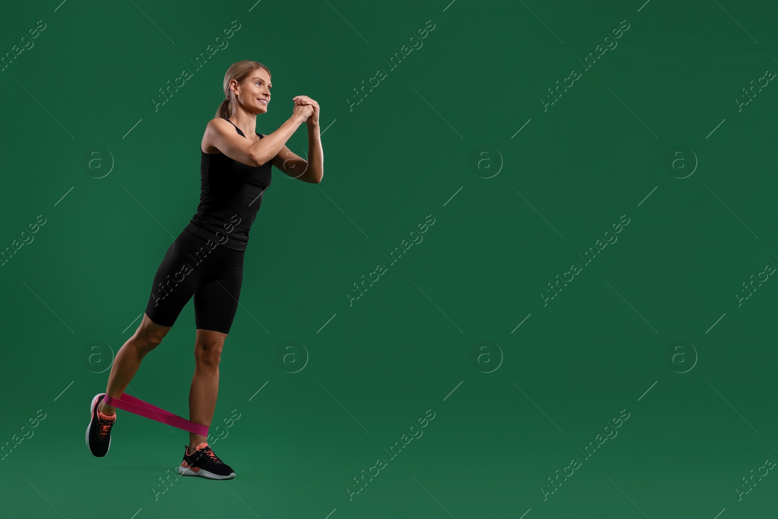 Photo of Smiling woman exercising with elastic resistance band on green background, low angle view. Space for text