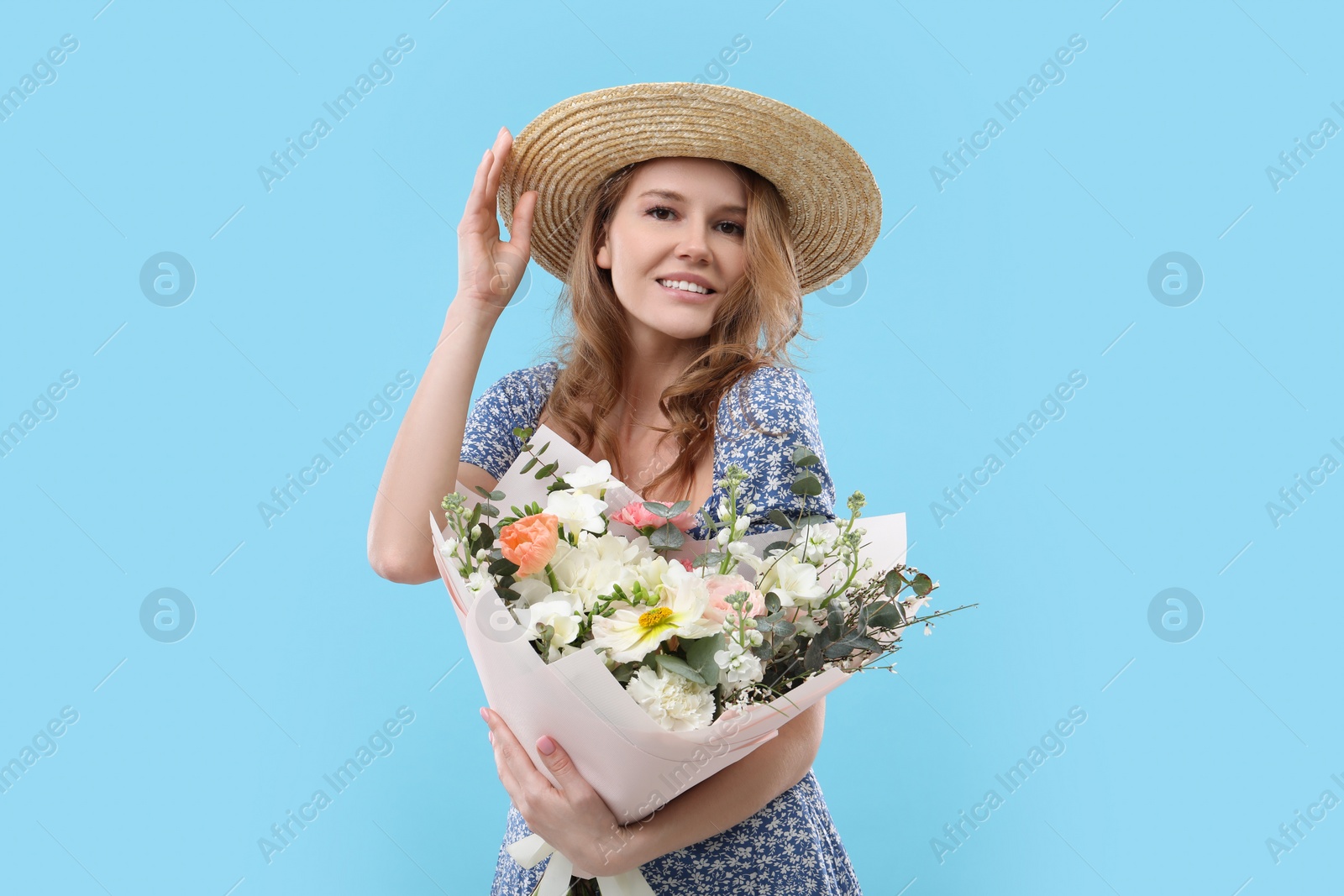 Photo of Beautiful woman in straw hat with bouquet of flowers on light blue background