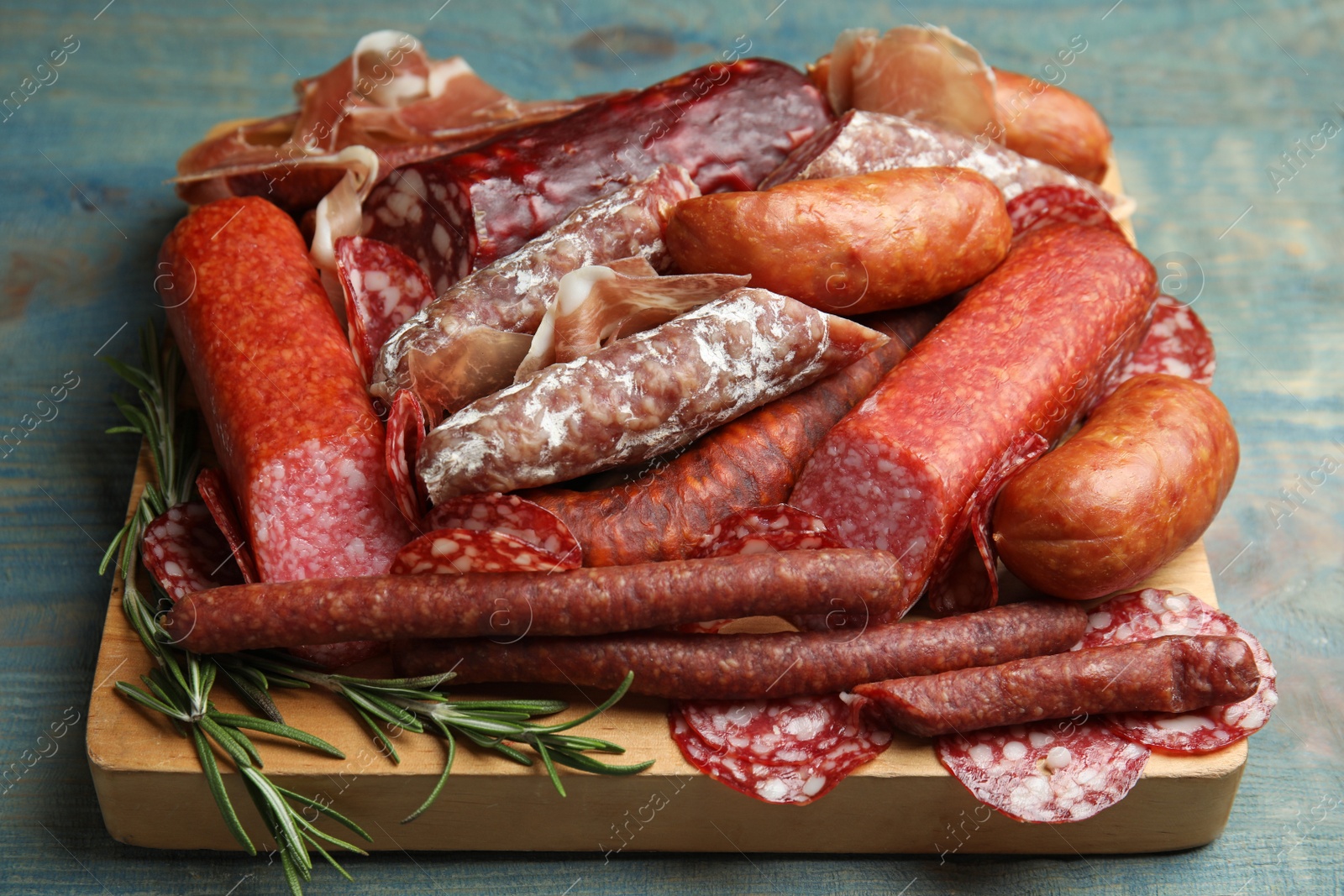 Photo of Different types of sausages served on light blue wooden table, closeup