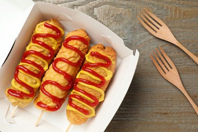 Delicious corn dogs with mustard and ketchup on wooden table, flat lay