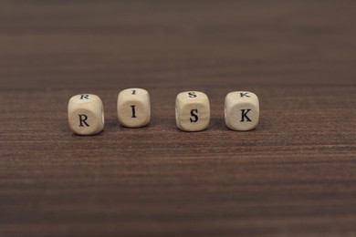 Photo of Cubes with word Risk on wooden table, closeup
