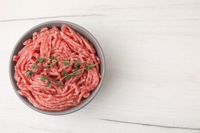 Photo of Fresh raw ground meat and thyme in bowl on white wooden table, top view. Space for text