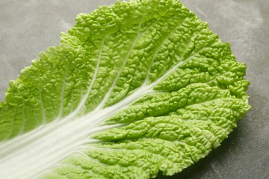 Photo of Fresh Chinese cabbage leaf on gray textured table, closeup