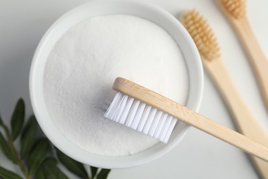 Photo of Bamboo toothbrushes, bowl of baking soda and green leaves on white table, flat lay