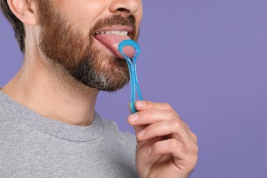 Photo of Man brushing his tongue with cleaner on violet background, closeup. Space for text