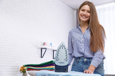 Young woman near board with iron and clothes at home. Space for text