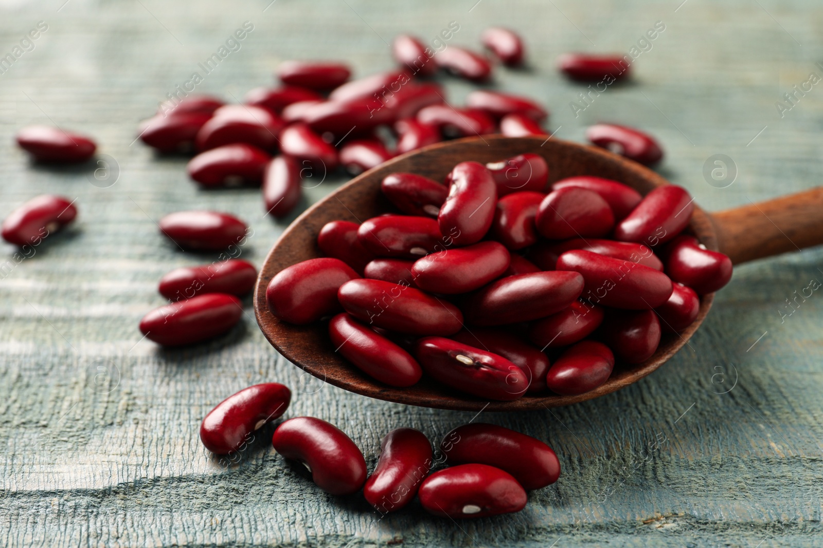 Photo of Raw red kidney beans with spoon on light blue wooden table, closeup