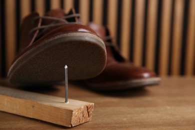 Metal nail in wooden plank and shoes on table, closeup