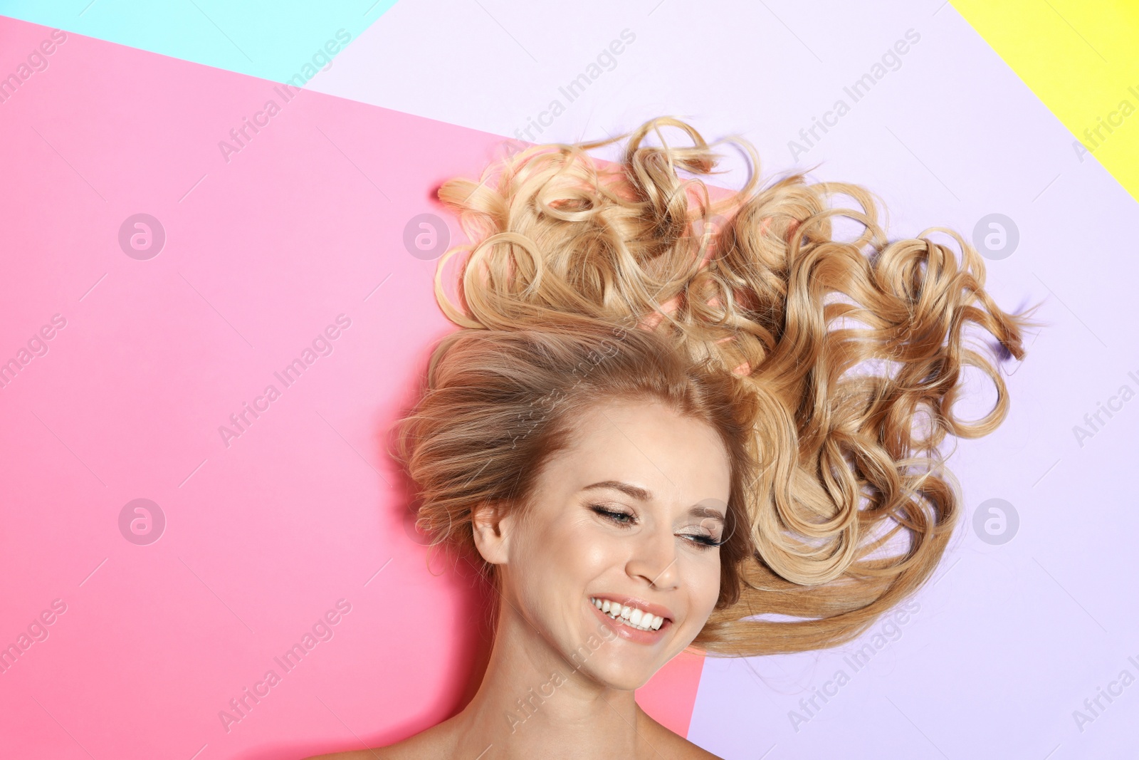 Photo of Beautiful woman with healthy long blonde hair on color background, top view