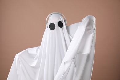 Person in ghost costume wearing headphones on dark beige background