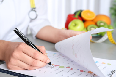 Photo of Female nutritionist with list of products at table, closeup