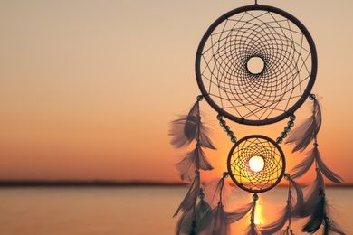 Photo of Beautiful handmade dream catcher near river at sunset. Space for text