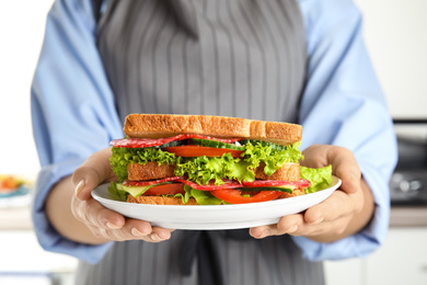 Photo of Woman holding plate with tasty sandwiches on light background, closeup