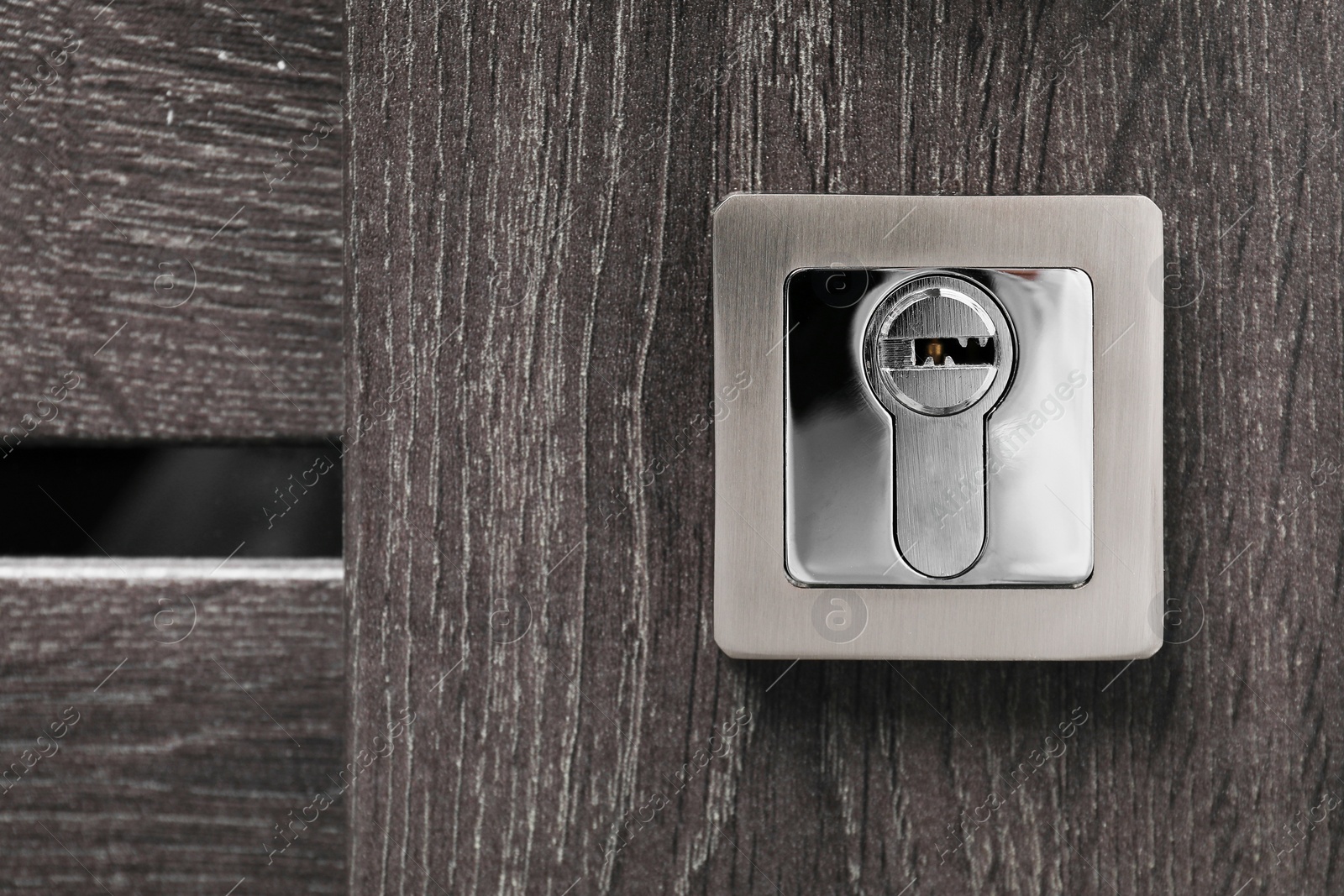 Photo of Metal keyhole on dark wooden door, closeup