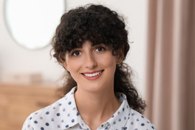 Portrait of beautiful woman with curly hair indoors. Attractive lady smiling and looking into camera