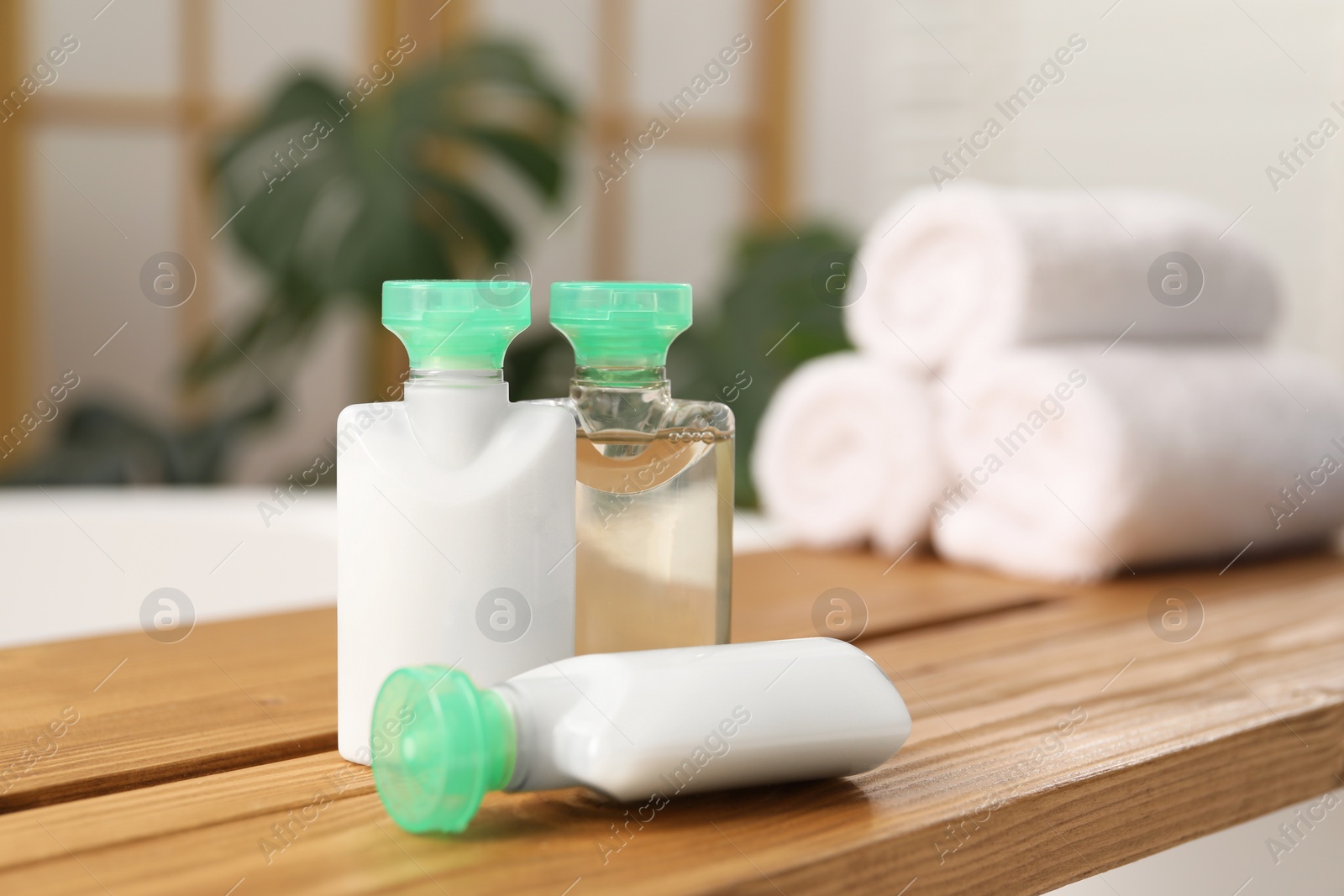 Photo of Wooden tray with mini bottles of cosmetic products on bath tub in bathroom