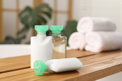 Photo of Wooden tray with mini bottles of cosmetic products on bath tub in bathroom