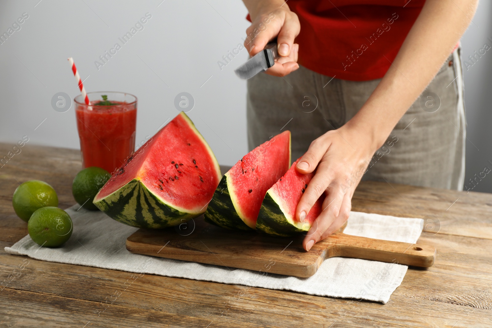 Photo of Woman cutting delicious watermelon at wooden table against light background, closeup