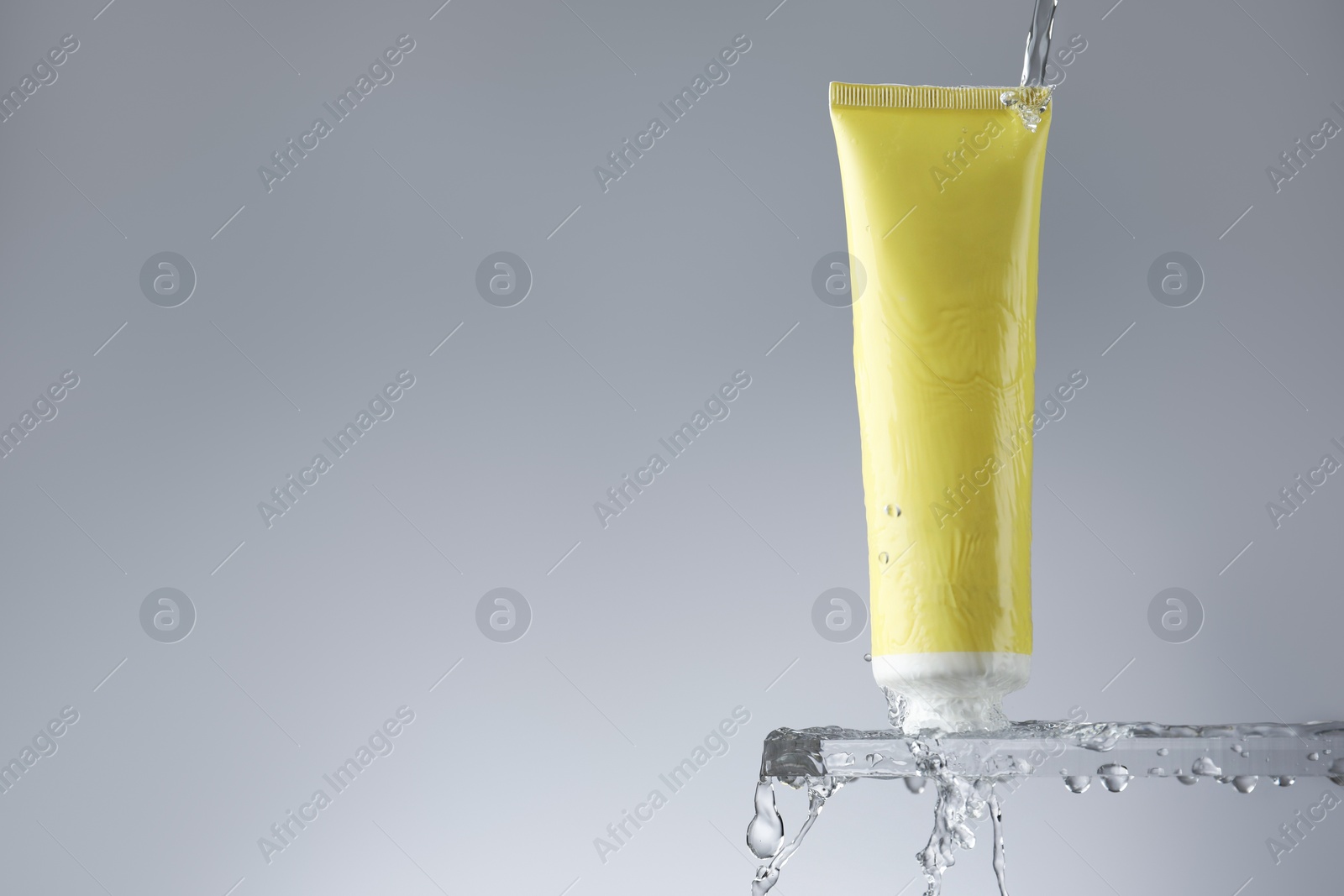 Photo of Moisturizing cream in tube on glass with water drops against grey background. Space for text