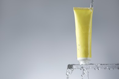 Photo of Moisturizing cream in tube on glass with water drops against grey background. Space for text