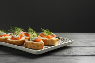 Photo of Tasty canapes with salmon, cucumber, cream cheese and dill on wooden table. Space for text
