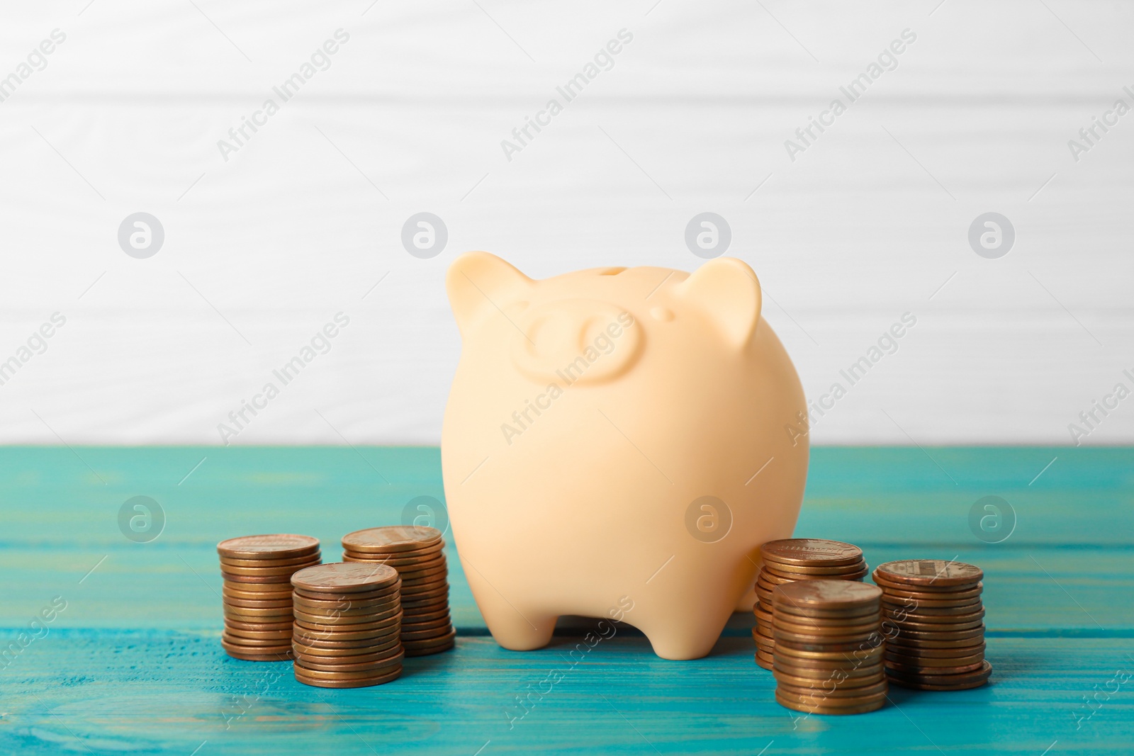 Photo of Ceramic piggy bank and coins on turquoise wooden table