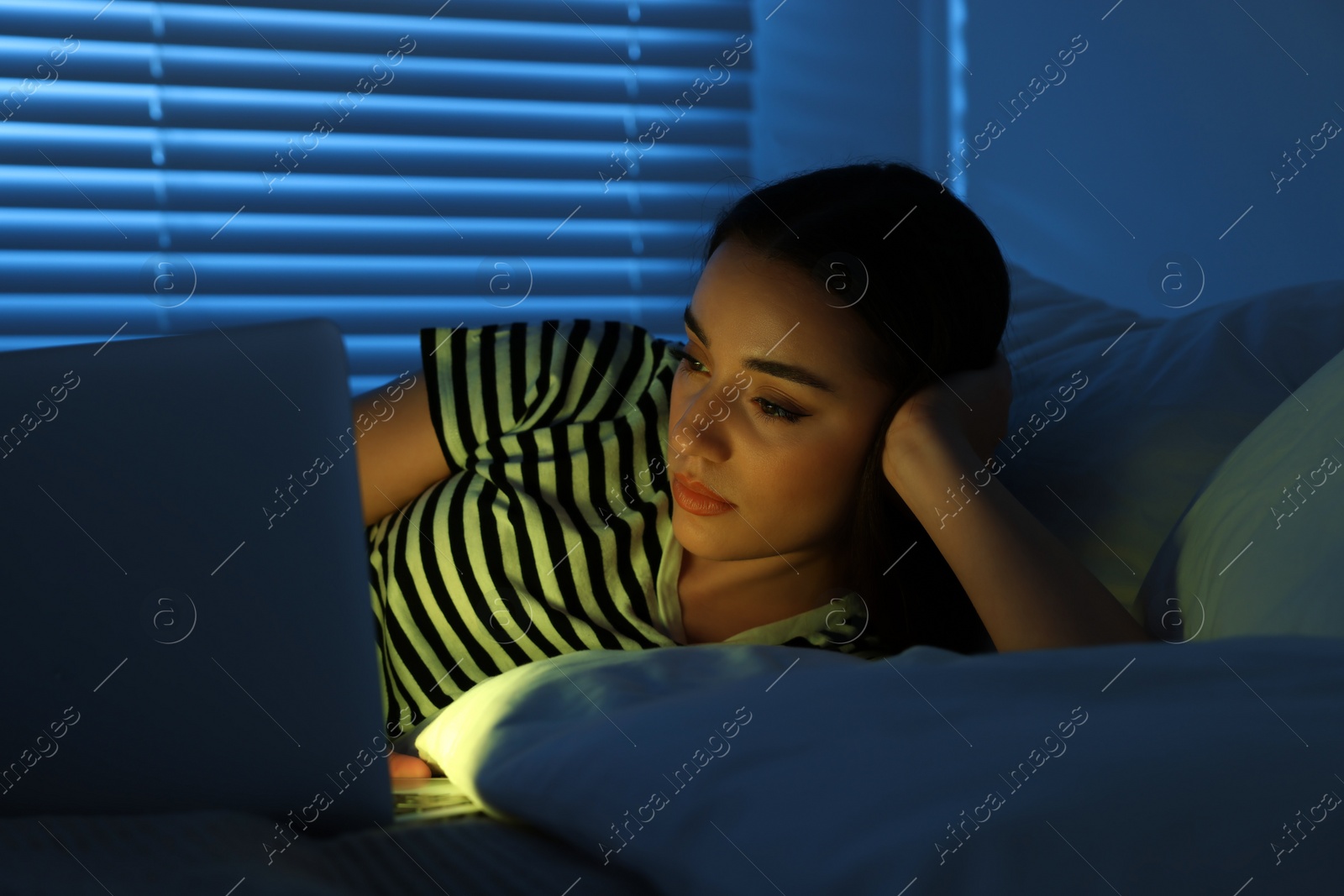 Photo of Young woman using laptop on bed at night. Internet addiction