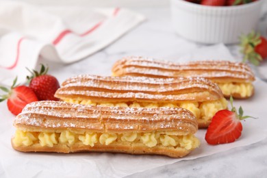 Delicious eclairs filled with cream and strawberries on white marble table