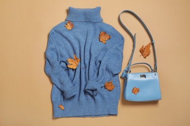 Sweater, bag and dry leaves on beige background, flat lay. Autumn season