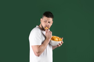 Greedy man hiding bowl with chips on green background
