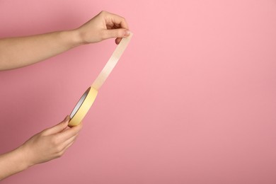 Photo of Woman holding beige adhesive tape on pink background, closeup. Space for text