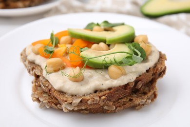 Tasty vegan sandwich with avocado, chickpeas and bell pepper on white plate, closeup